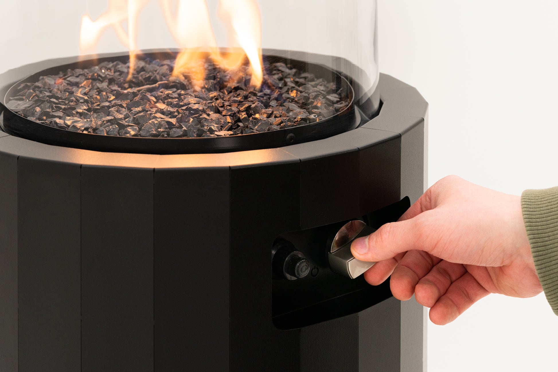 Een hand draait de knop om de vlam van de Bino buitenhaard aan te steken voor precieze warmtecontrole.