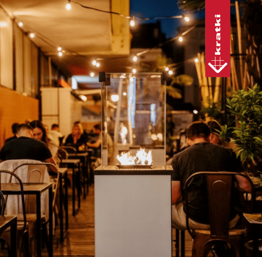 Kratki PATIO Slim gasgestookte terrasverwarmer met echt vuur op een restaurantterras in de avond