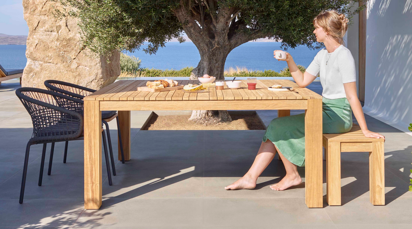 ardinico Tecca tuintafel in gebruik – een ontspannen zomerochtendontbijt op het terras, met natuurlijke teakhouten afwerking en luxe uitstraling.
